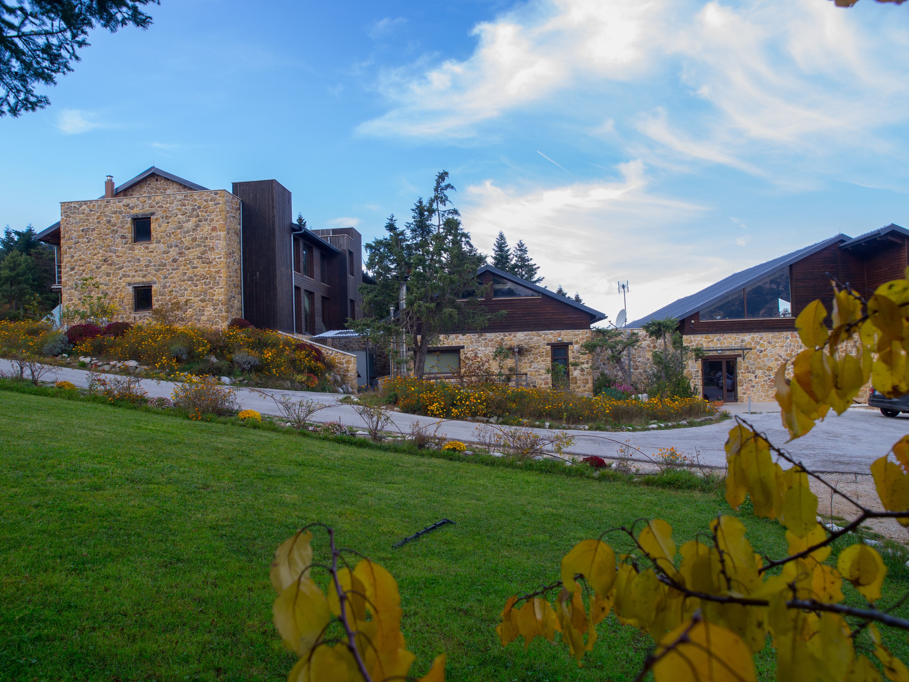 A modern building with stone and wood exterior, surrounded by a well-maintained lawn and flowering plants.