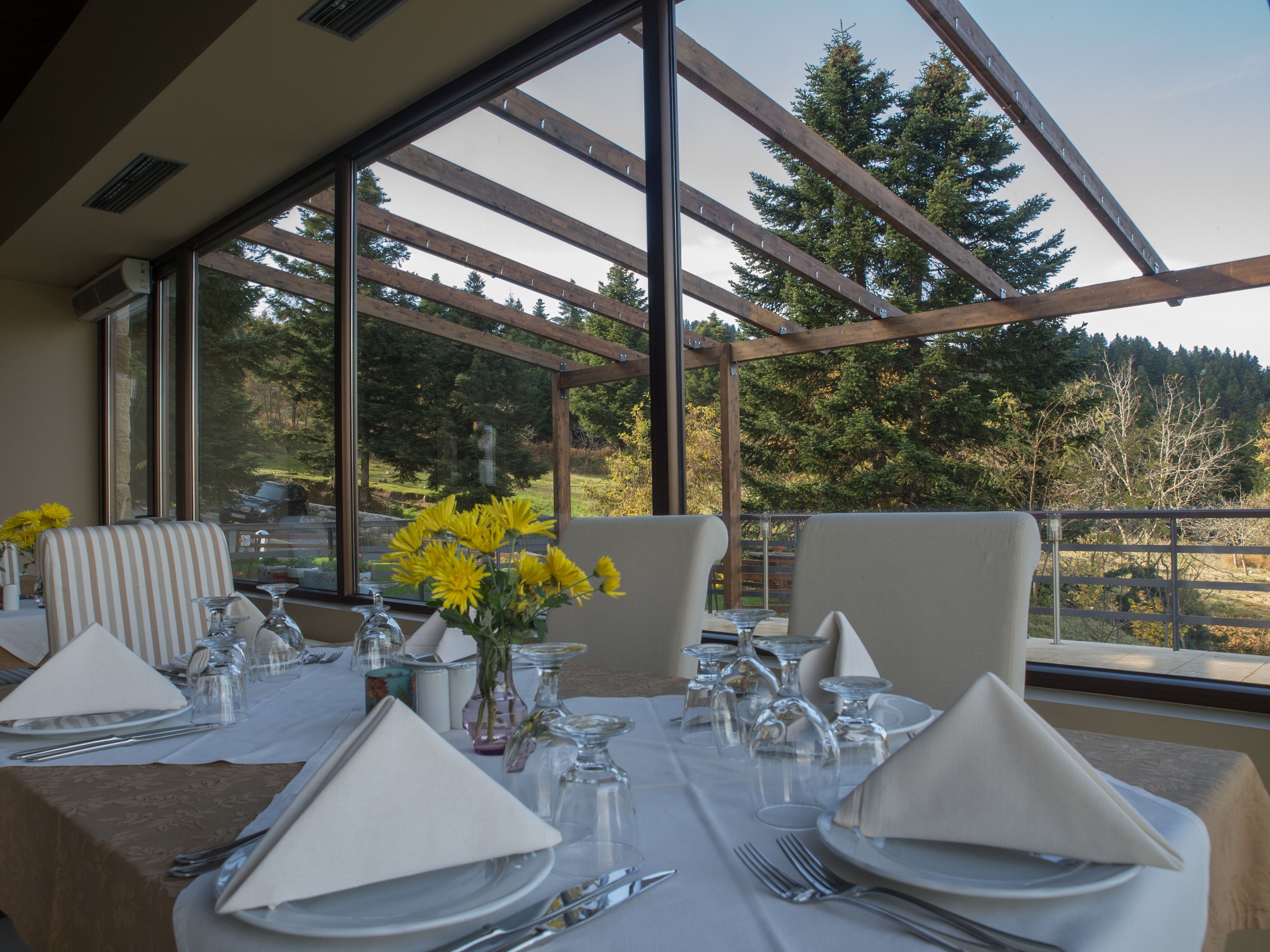 A dining area with a table set for four, large windows, and a view of trees and a car outside.