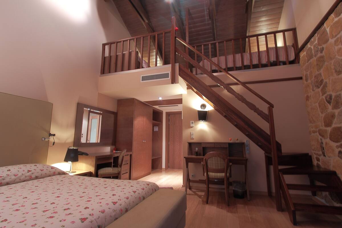 Quarto com cama, escrivaninha, cadeira, escada e uma pequena varanda.