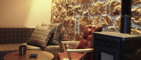 Un salon chaleureux avec un mur en pierre, une cheminée, un canapé, un fauteuil et une table.