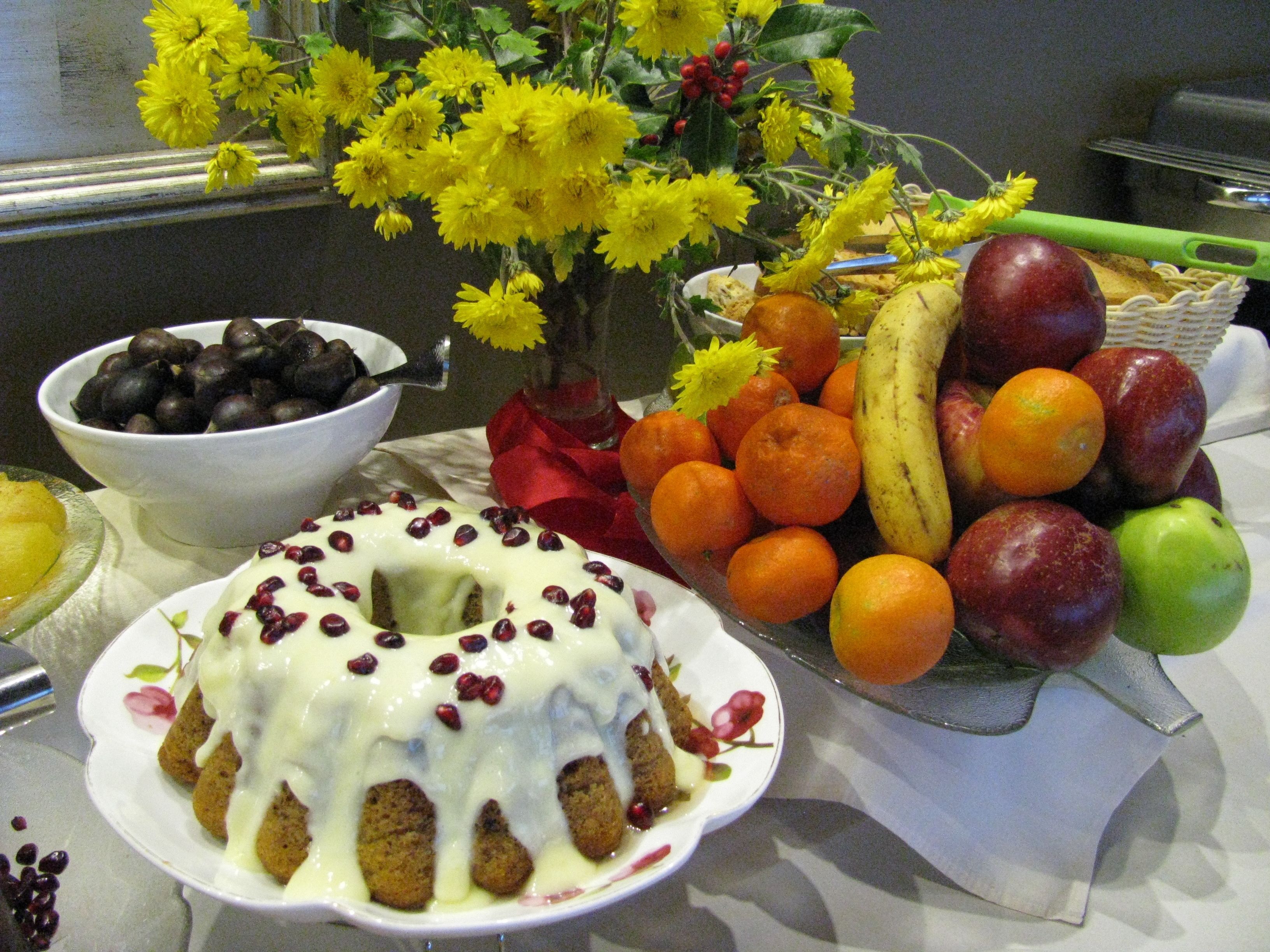 Una mesa con frutero, cesta de fruta y postre.