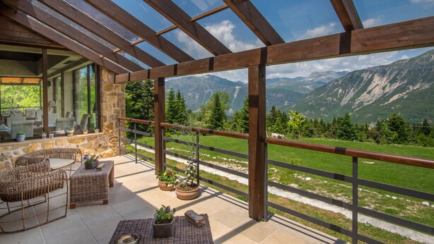 Un espace extérieur abrité, aménagé avec des meubles en osier, des murs en pierre et offrant une vue sur les montagnes.