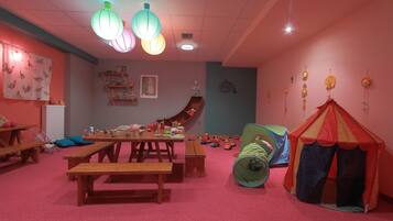 Una sala de juegos infantil con bancos de madera, un tobogán y una tienda de campaña.