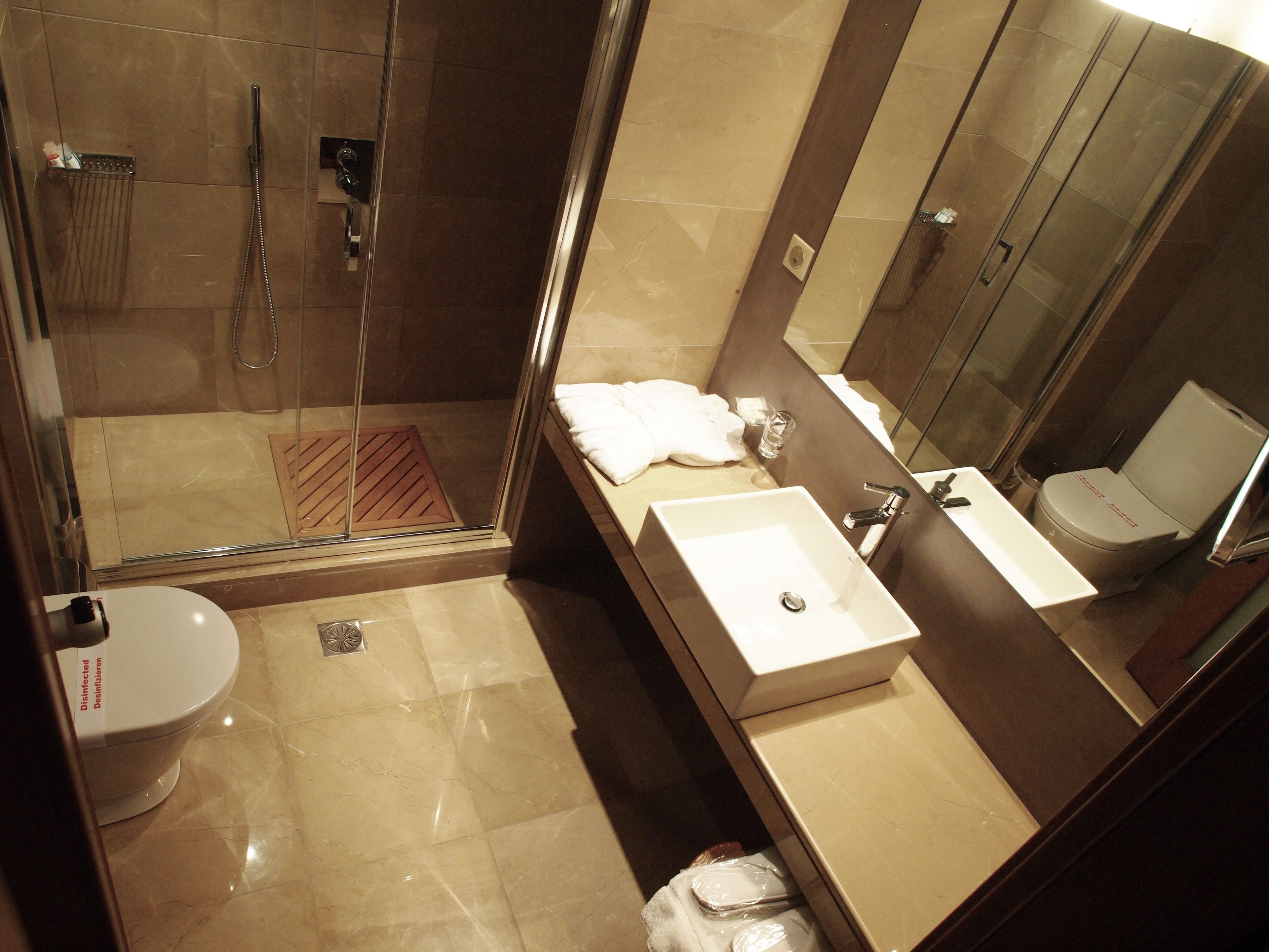 A modern bathroom with a glass-enclosed shower, a standalone toilet, and a vanity with a sink and mirror.