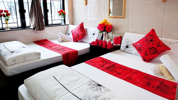A hotel room with two beds, a window with curtains, a vase with flowers, and a wall-mounted mirror. - Day And Night Hotel - Hostel (Kowloon)