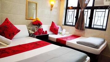 A hotel room with two beds, each with a red bedspread and pillows, a vase of flowers, and a window with curtains.