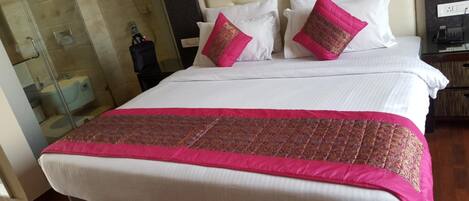 A hotel room with a bed, two pillows, a nightstand, and a glass shower enclosure.