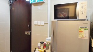 Une chambre d’hôtel avec une porte en bois sombre, un panneau de signalisation indiquant la sortie, un réfrigérateur muni d’une étiquette indiquant sa consommation énergétique et un four à micro-ondes posé sur le dessus.