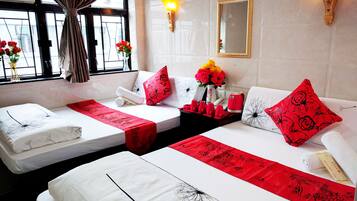 A hotel room with two beds, a window with curtains, a vase with flowers, and a wall-mounted mirror.