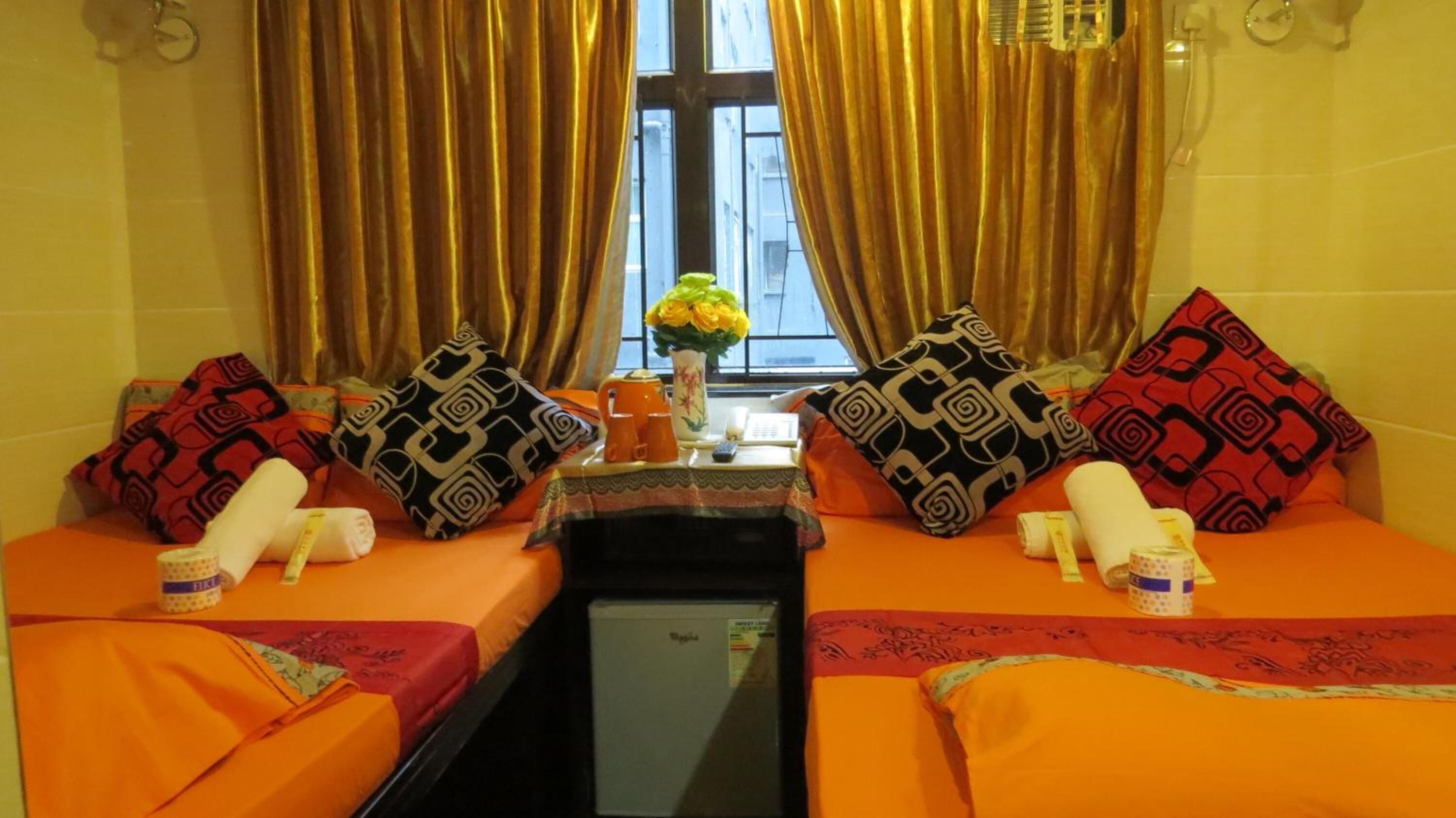A hotel room with two beds, a small table with a vase of flowers, and a window with curtains.