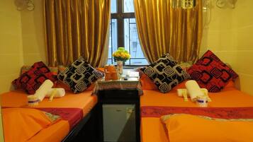 A hotel room with two beds, a small table with a vase of flowers, and a window with curtains.