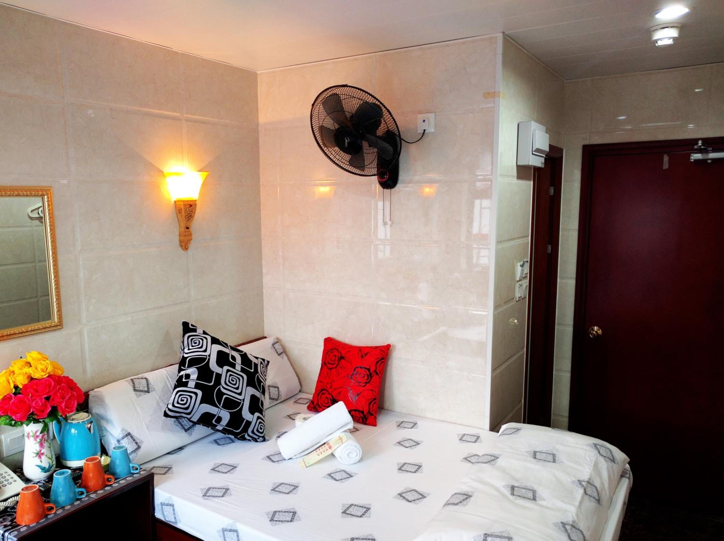 A hotel room with a bed, a wall-mounted fan, a mirror, and a door.