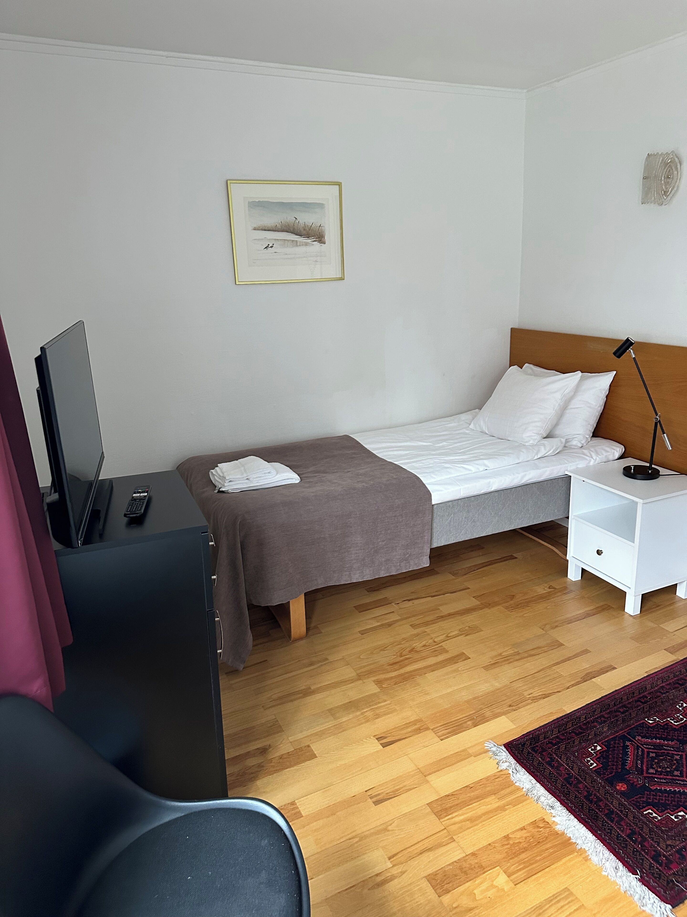A bedroom with a bed, bedside table, lamp, and a painting on the wall.