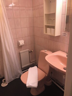 A bathroom with a toilet, a sink, a shower curtain, and a toilet paper holder. - Värdshuset Hwitan (Falkenberg)