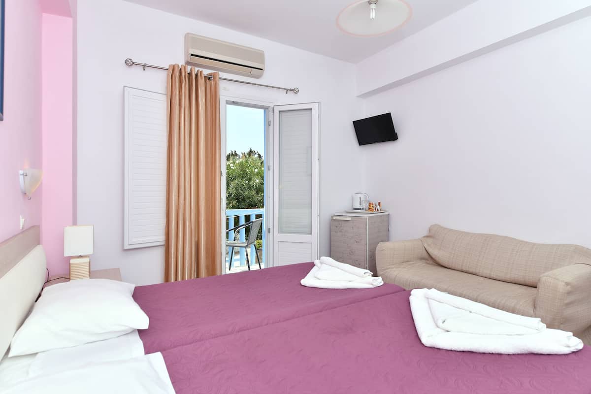 Una habitación de hotel con cama, sofá, televisión y aire acondicionado.