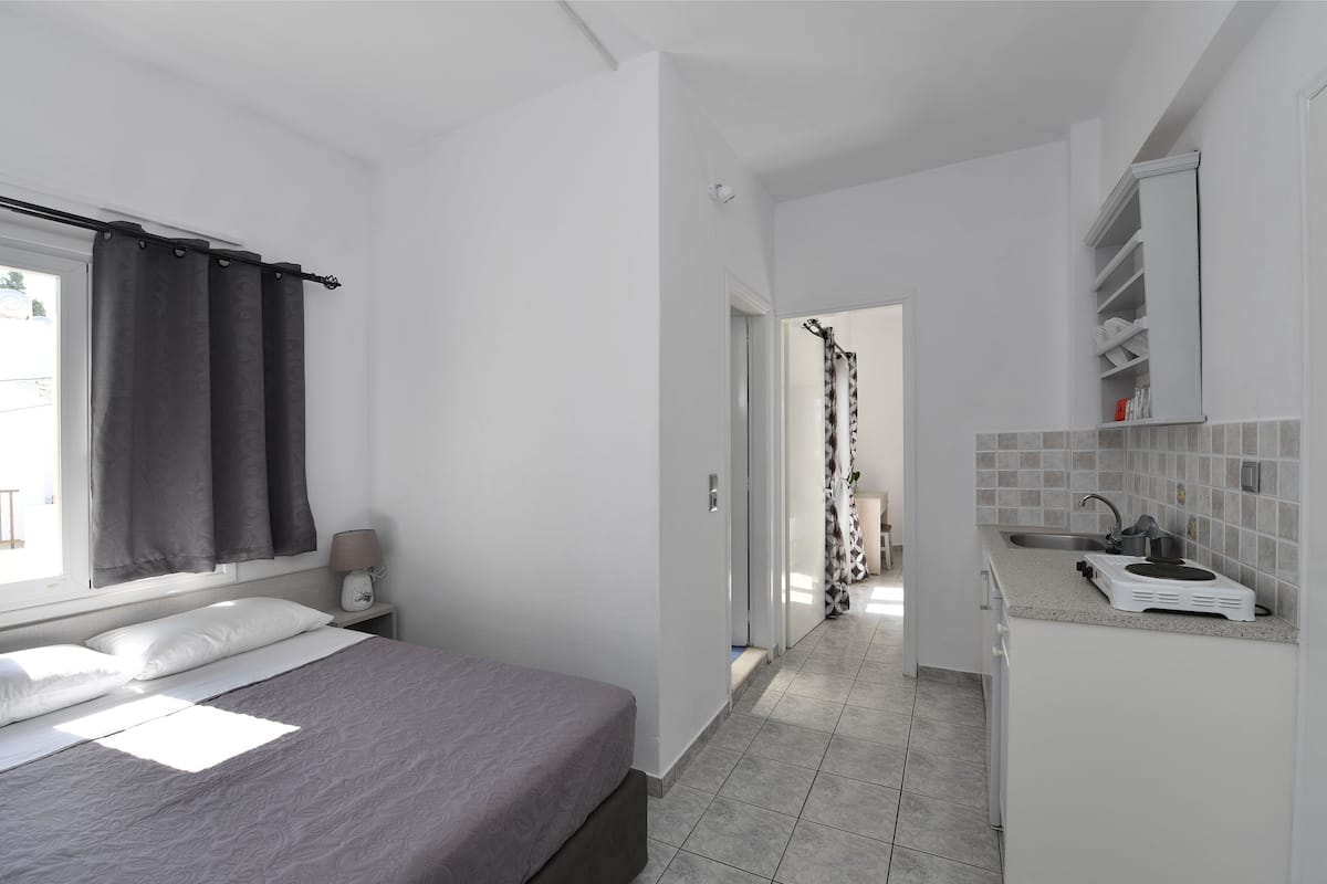 Una habitación de hotel moderna con cama, mesita de noche, ventana con cortinas, baño con cortina de ducha y kitchenette con fregadero y estufa.