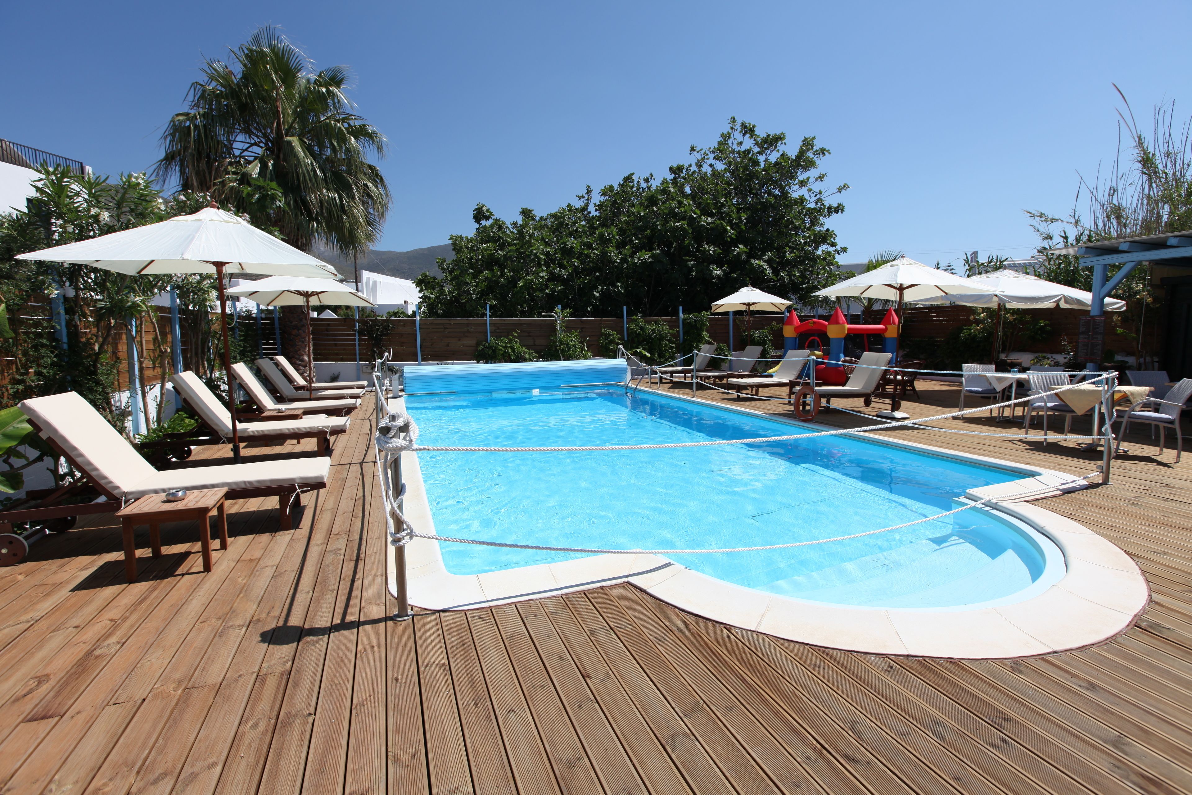 Una terraza de madera con piscina, sillas de descanso y sombrillas.