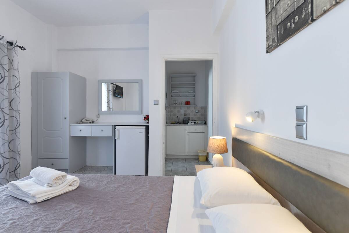 Una habitación de hotel con cama, escritorio, kitchenette pequeño y baño.