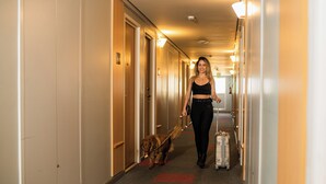 Een hotelgang met deuren, een persoon die een hond uitlaat, en bagage.