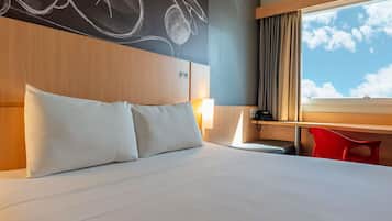 Een hotelkamer met een groot bed, een bureau, een stoel en een raam met uitzicht op de lucht.