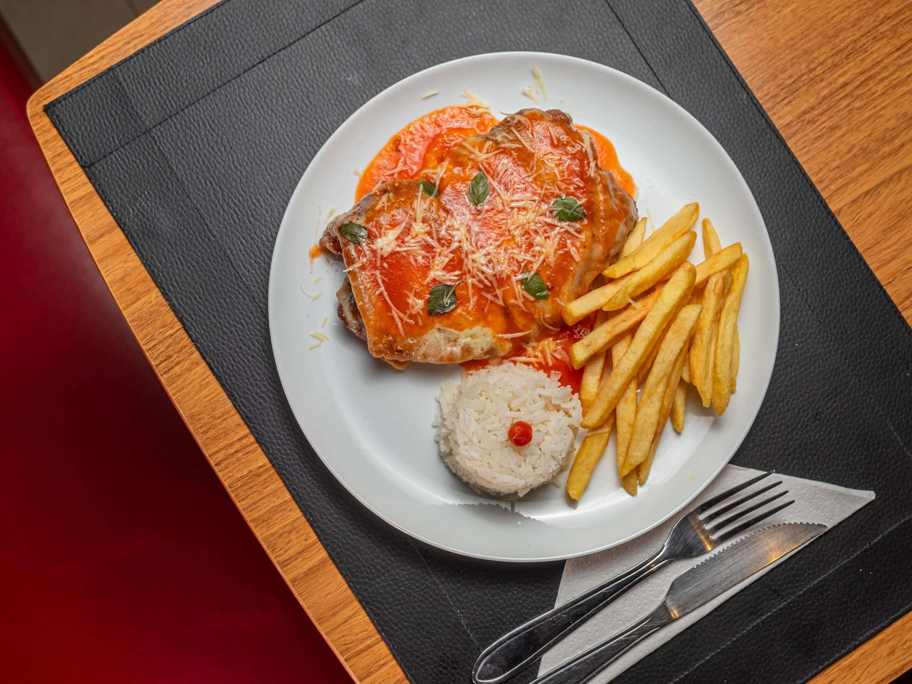 A plate with a meat dish, fries, and rice.