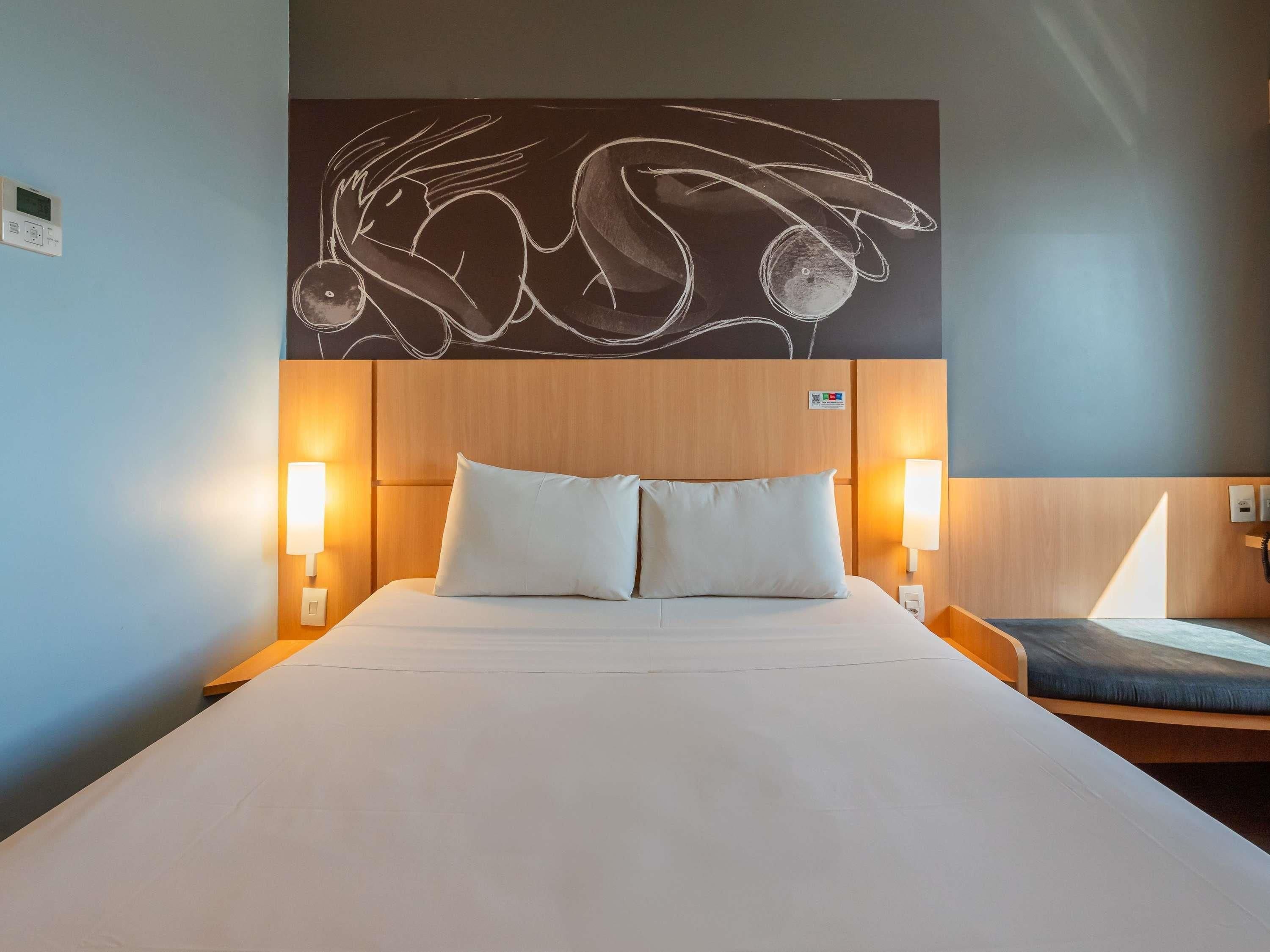 A hotel room with a large bed, two bedside lamps, a wooden headboard, and a wall art piece above the bed.