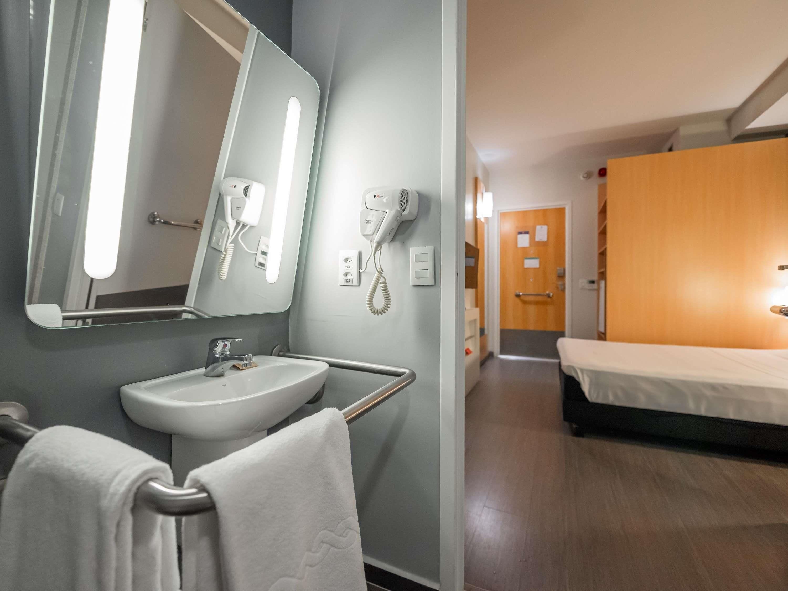Un baño de hotel con lavamanos, espejo, toallero y secador de pelo.