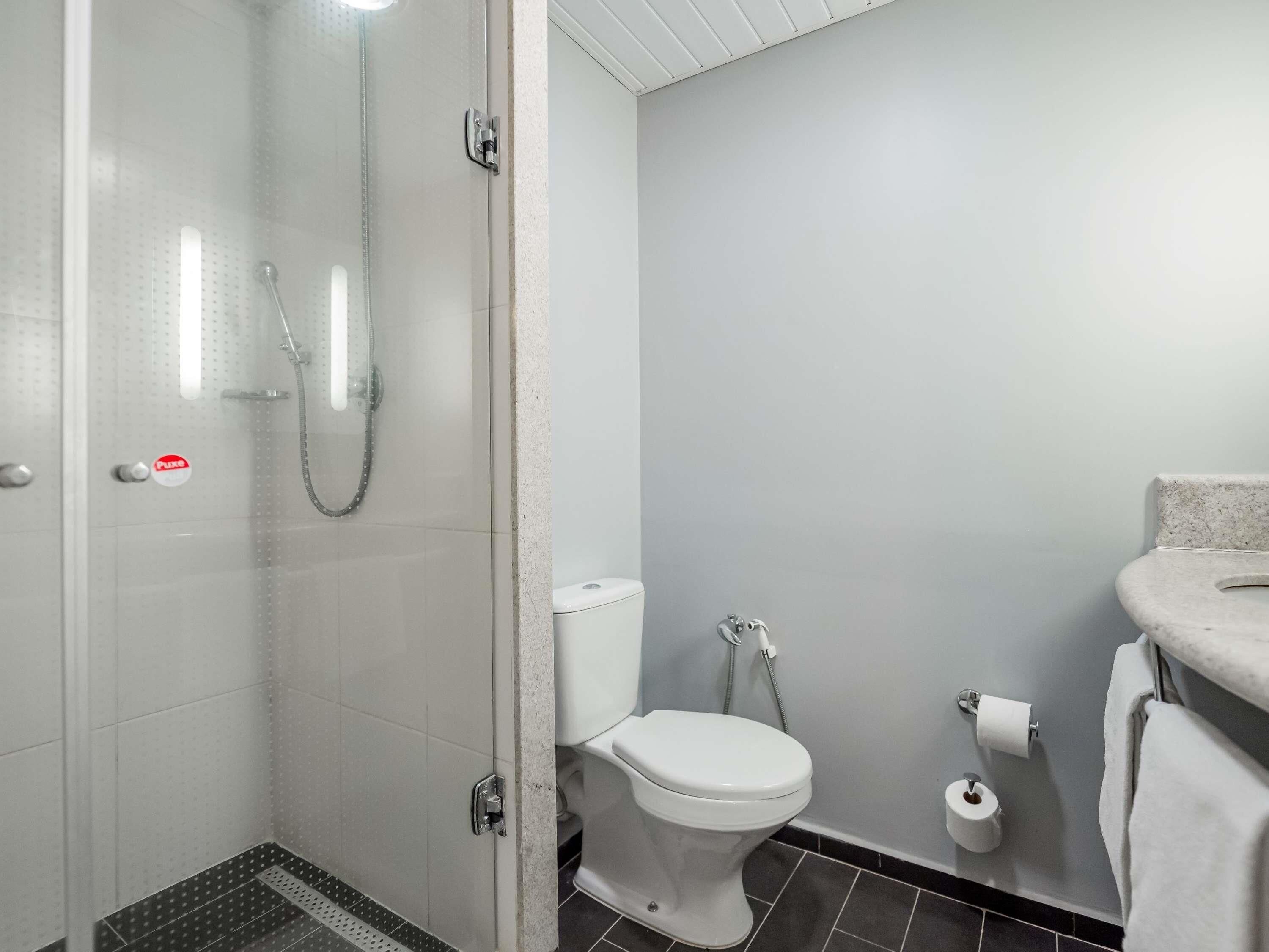 A bathroom with a glass shower enclosure, a toilet, and a sink with a towel.