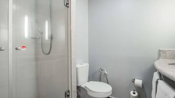 A bathroom with a glass shower enclosure, a toilet, and a sink with a towel.