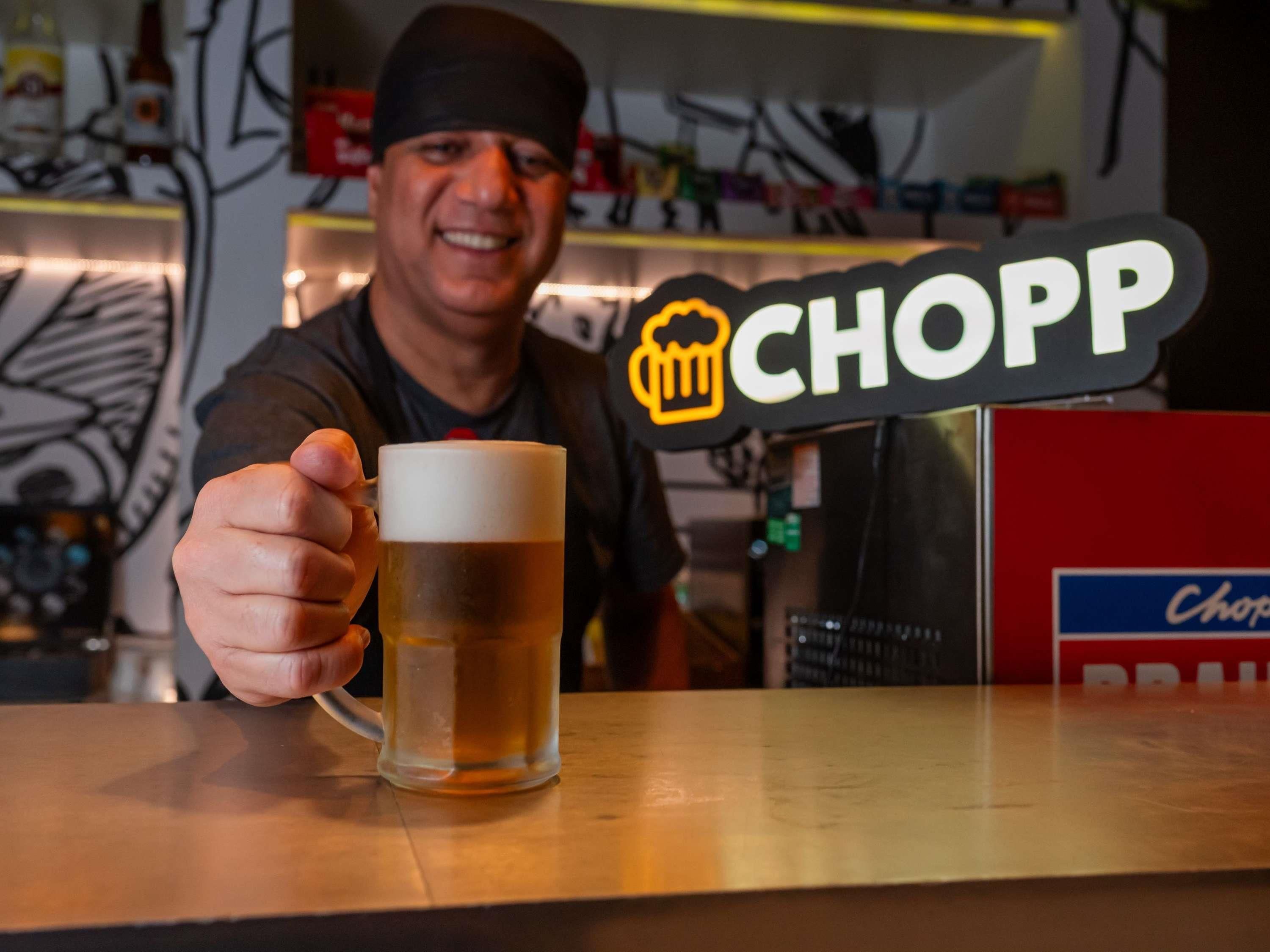 A person holding a beer mug with a sign that reads 'CHOPP' in the background.