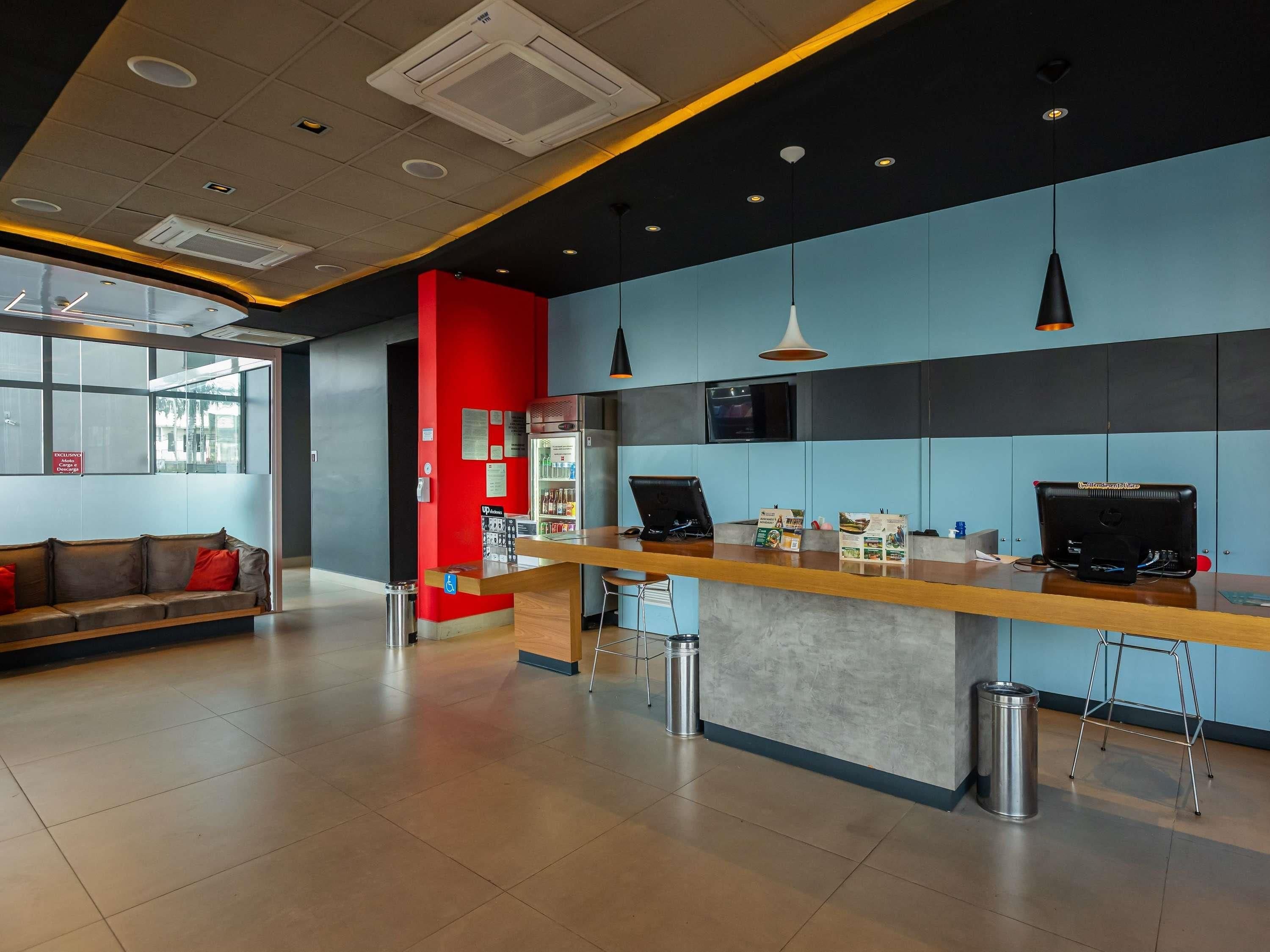 A modern hotel lobby with a reception desk, seating area, and a refrigerator stocked with beverages.