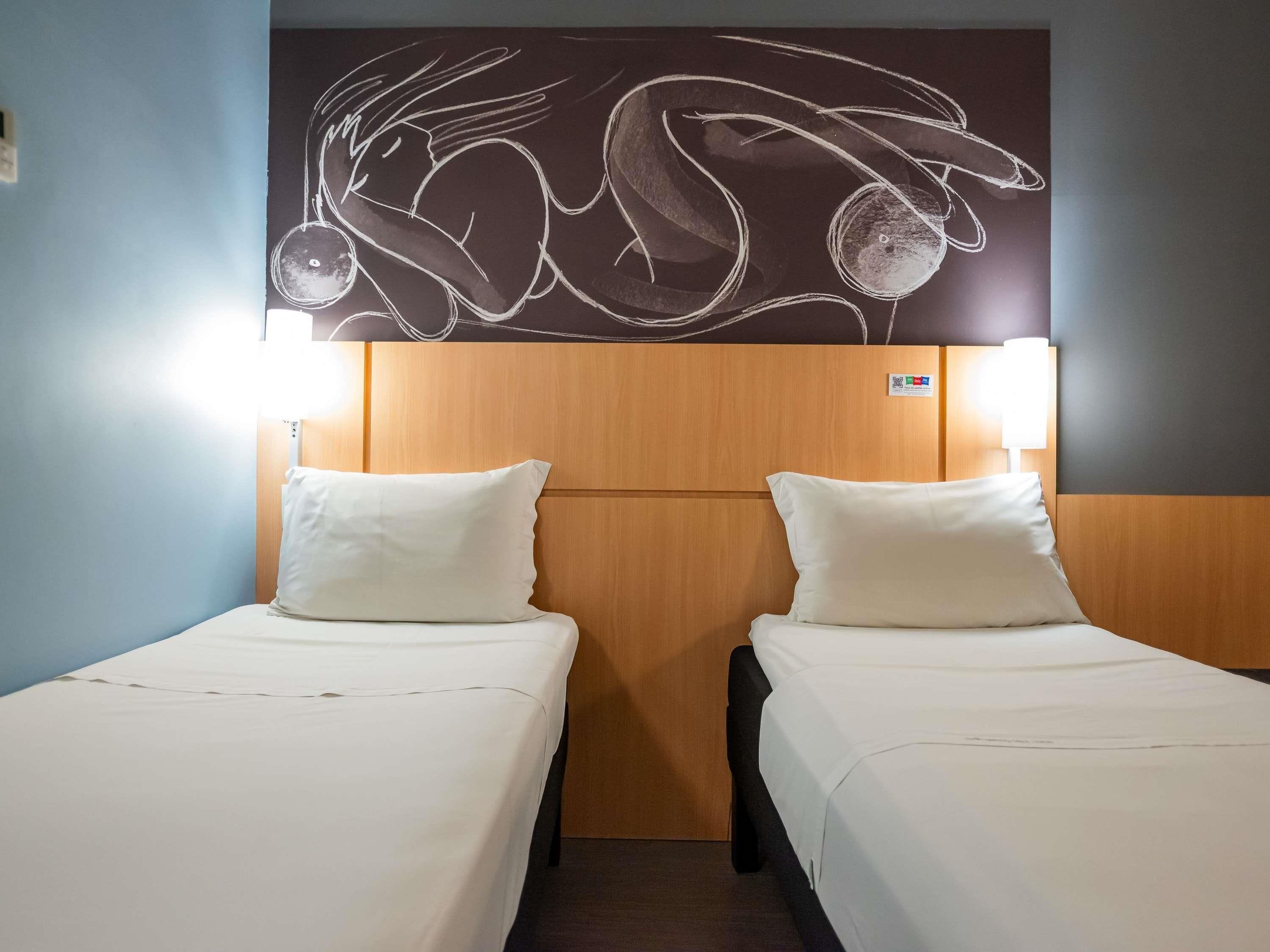 Une chambre d’hôtel avec deux lits, une tête de lit en bois et des œuvres d’art accrochées au mur au-dessus des lits.