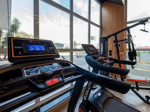 A gym with a treadmill, a stationary bike, and a digital display. - Ibis Guaratinguetá Aparecida (Guaratingueta)