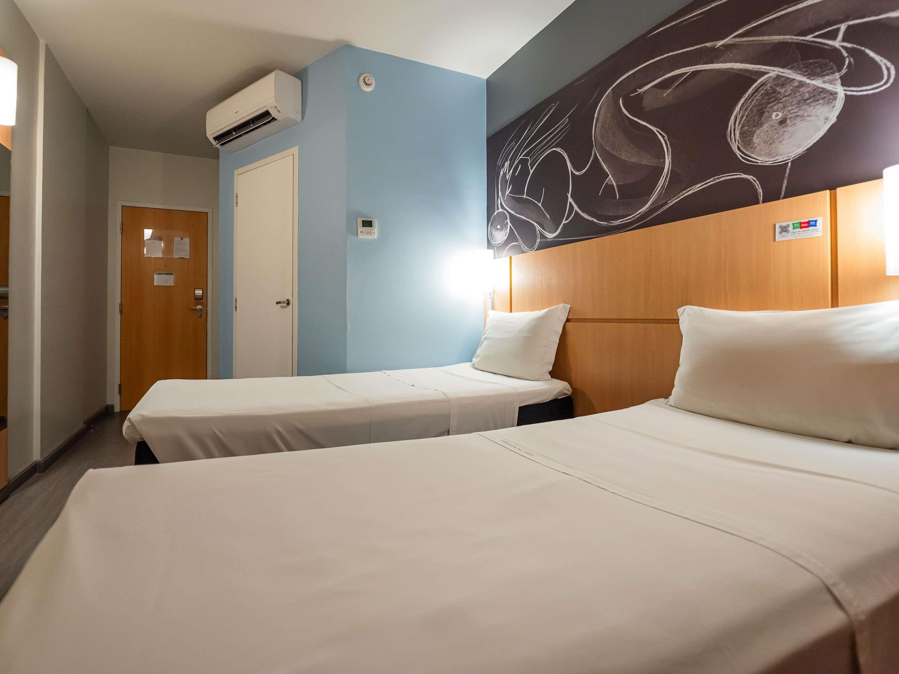 A hotel room with two beds, a wooden headboard, a blue accent wall, and a chalkboard with abstract art.