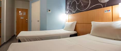 A hotel room with two beds, a wooden headboard, a blue accent wall, and a chalkboard with abstract art.