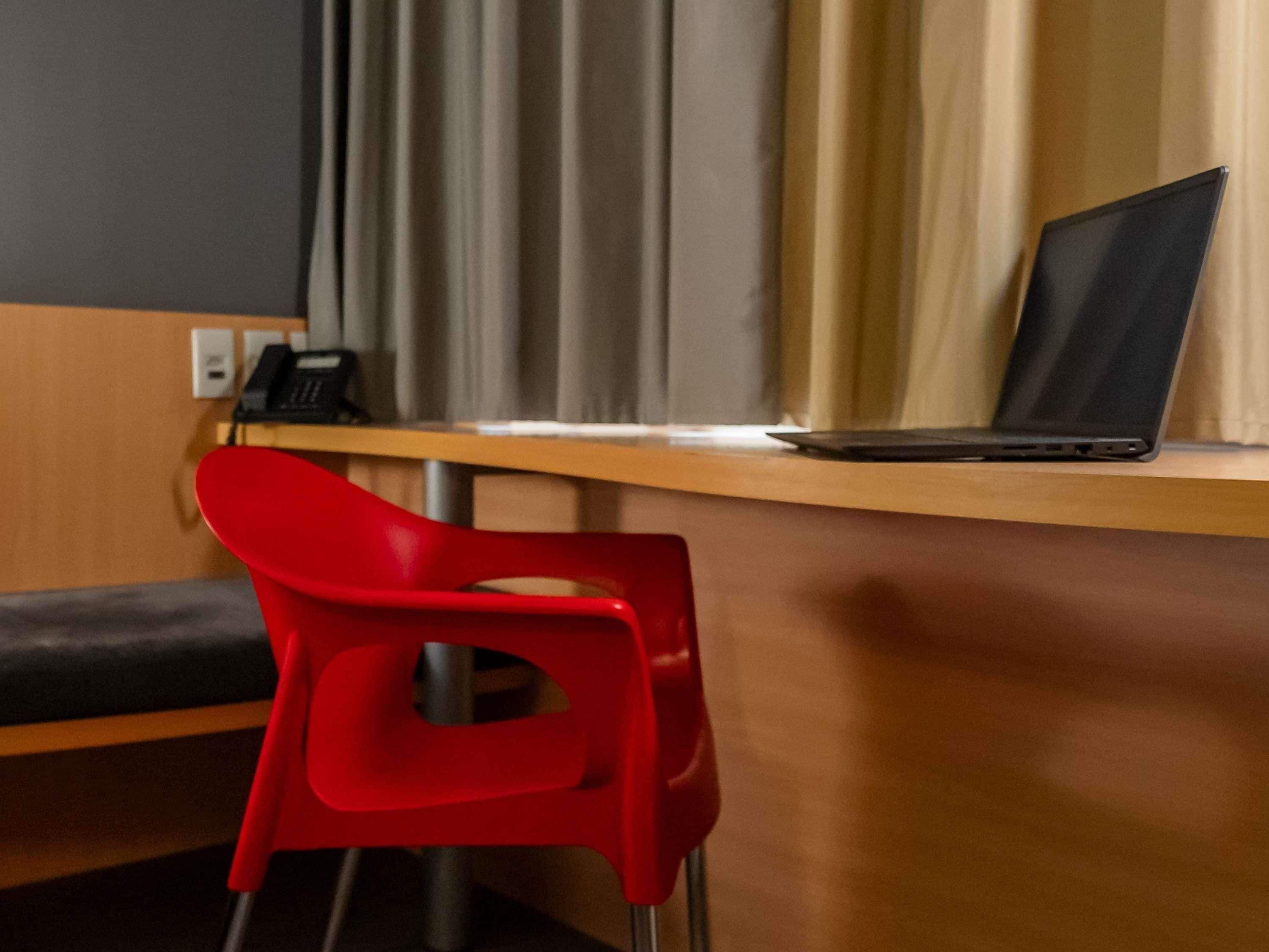 Une chambre moderne avec un bureau en bois, une chaise rouge et un ordinateur portable.