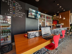 Un espace bar avec un ordinateur portable posé sur une table, un réfrigérateur rempli de boissons et un mur orné de texte.