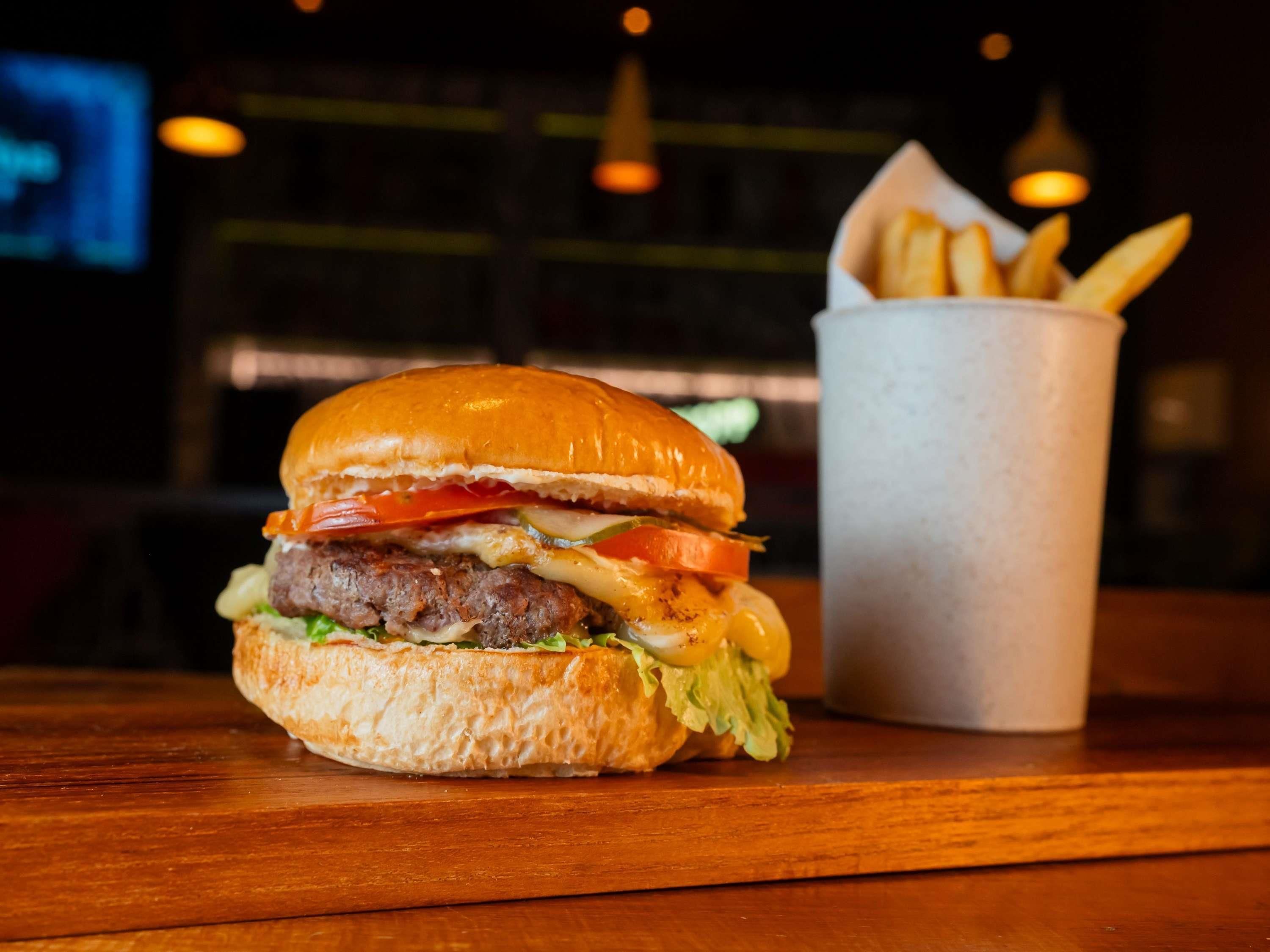 Una hamburguesa con lechuga, tomate y queso, junto a una porción de papas fritas sobre una mesa de madera.