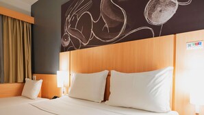 A hotel room with a large bed, two bedside lamps, a wooden headboard, and a wall mural. - Ibis Guaratinguetá Aparecida (Guaratingueta)