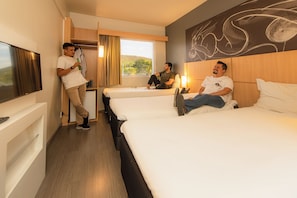 A hotel room with two beds, a TV, and a window with a view of the outdoors. - Ibis Guaratinguetá Aparecida (Guaratingueta)