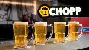 Vier bierglazen op een bar, met een neonreclame op de achtergrond.