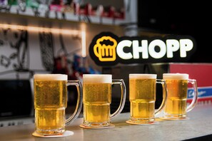 Cuatro vasos de cerveza sobre una barra, con un letrero de neón al fondo.