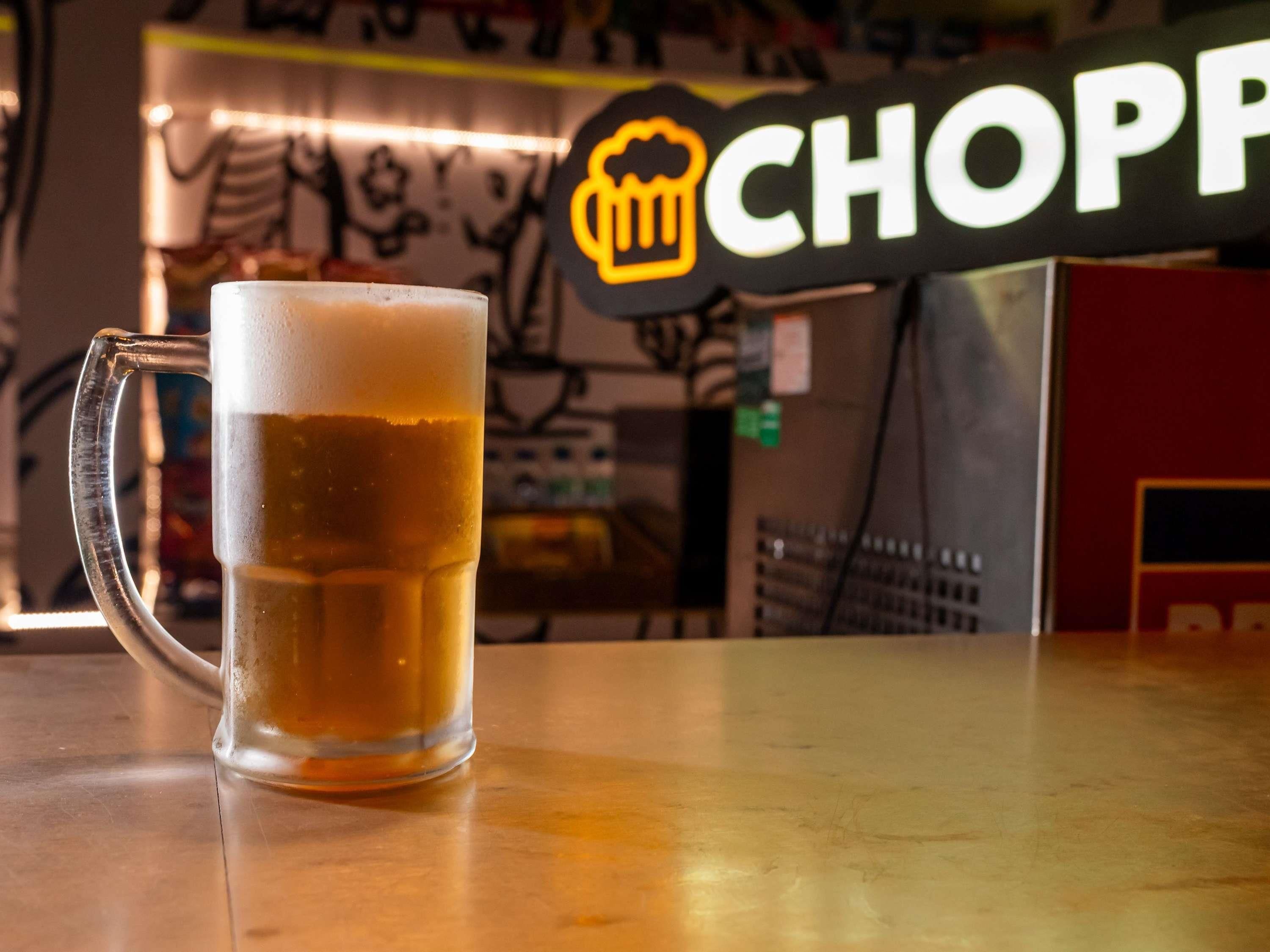 A glass of beer on a bar counter with a 'CHOPP' sign in the background.