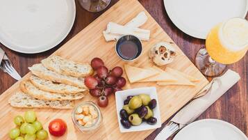 Een houten tafel met diverse soorten eten, zoals brood, druiven, olijven en een salade.