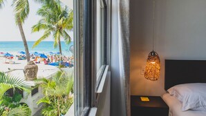 Habitación de hotel con vista a la playa, una cama, una mesita de noche y una lámpara colgante.