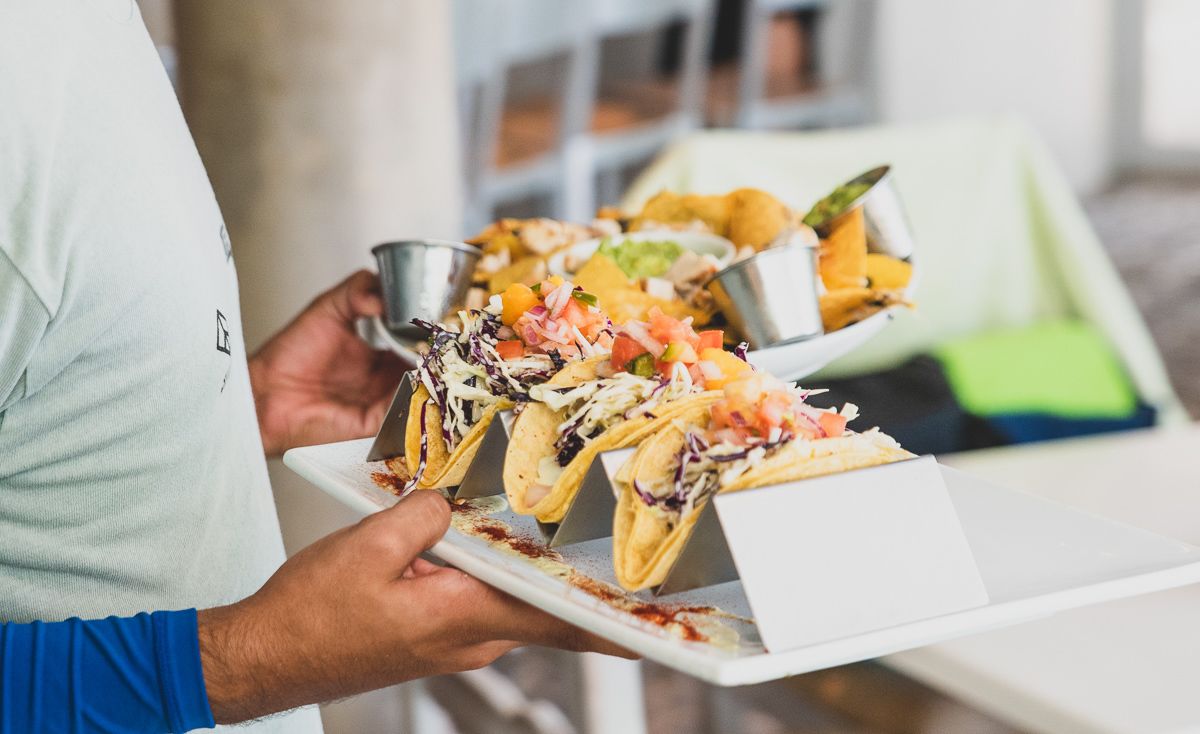 A person holding a tray with nachos and tacos.