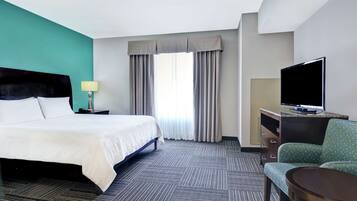 A hotel room with a bed, a desk with a TV, a chair, and a window with curtains.