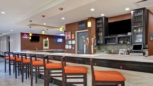 Eine Bar mit Theke, Barhocker, Fernseher und einer Auswahl an Gläsern und Flaschen.