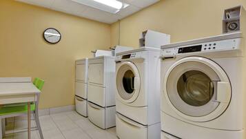 A laundry room with multiple washing machines, a clock on the wall, and a table with chairs.