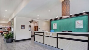 Ein Hotel-Empfangsbereich mit modernem Design, der einen Empfangstresen, eine grüne, strukturierte Wand und eine große dekorative Leuchte zeigt.